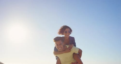 4k video footage of a young couple bonding on the beach and giving each other a piggyback ride