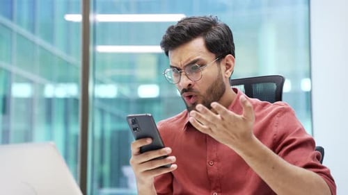 Concerned Young Man Using Smartphone in Modern Office