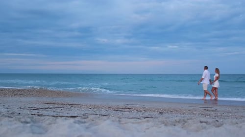 Romantic Couple Walking Along a Misty Shoreline with Calm Ocean Waves and a Cloudy Sky