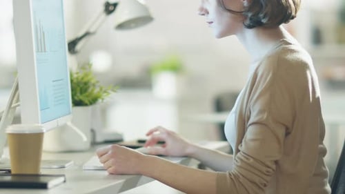 Young Beautiful Woman Works at Her Desktop Computer. Sitting at Her Desk in a Light and Modern Offi
