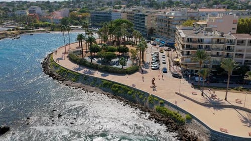 Aerial drone view of Antibes seafront promenade, curved walkway lined with palm trees, overlooking t