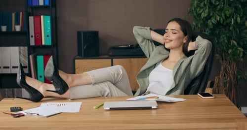 Calm Beautiful Adorable Woman Sitting at Table in Office Holds Legs on Table Relaxes After Hard