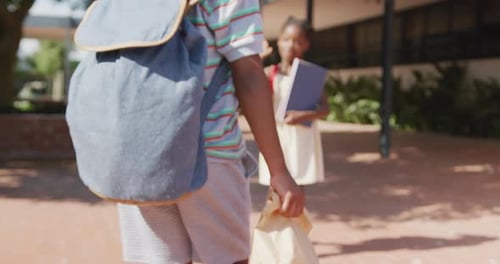 Video of happy african american boy and girl with schoolbags high fiving outside school