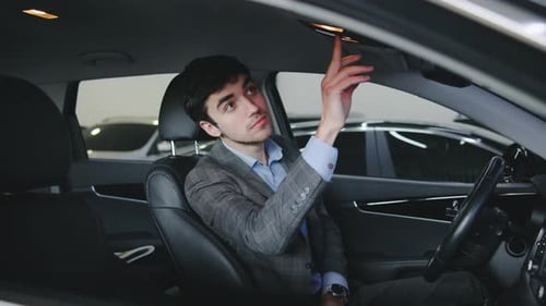 Young Man Gestures Positively While Sitting Inside a Car at a Dealership in the Morning Expressing