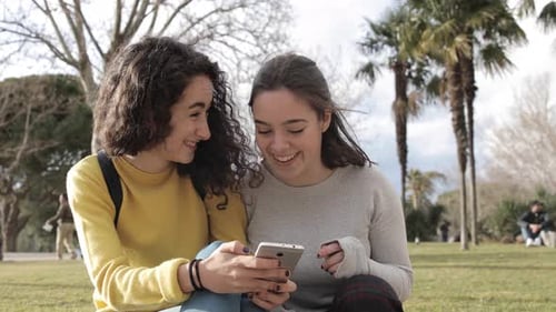 Two beautiful girls using smartphone at park and sharing on social media