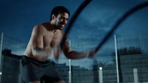 Shirtless man intensely exercising with ropes in an urban setting
