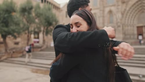 Young couple embracing in front of cathedral on cloudy day.