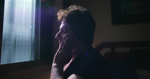 Senior Woman Sits By Window with Sadness