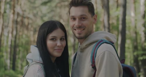 Portrait of Happy Young Couple Standing in Green Forest with Backpacks Smiling Looking at Camera