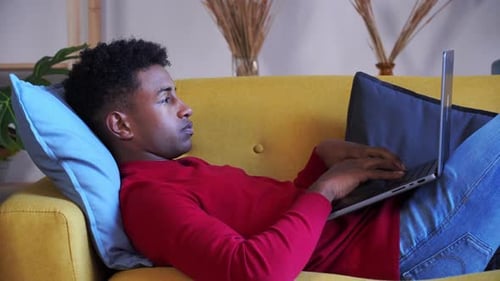 Young Adult Lying on Couch Using Laptop