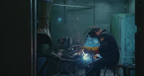 Man Welding Metal in a Dark Factory