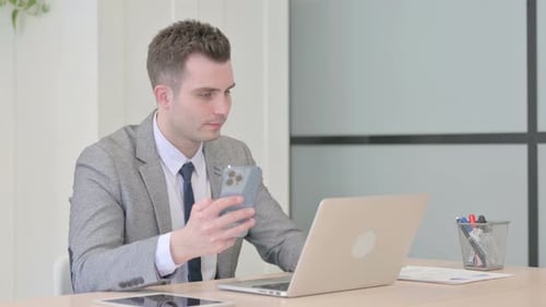 Man Using Smartphone While Working on Laptop