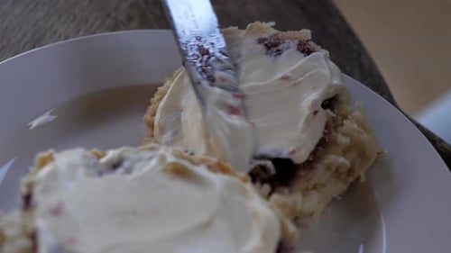 Personne étalant de la crème épaisse fouettée sur un scone à la confiture traditionnel fait maison avec une plaque en métal argenté