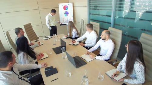 Top View of Young Male Manager Presenting Project Plan to Colleagues in Meeting Explaining Report