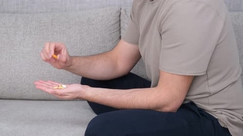Person Holding Pills in Hand On Couch