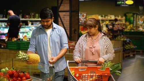 Young Indian Couple Choosing Discounted Fresh Pineapple in a Grocery Store