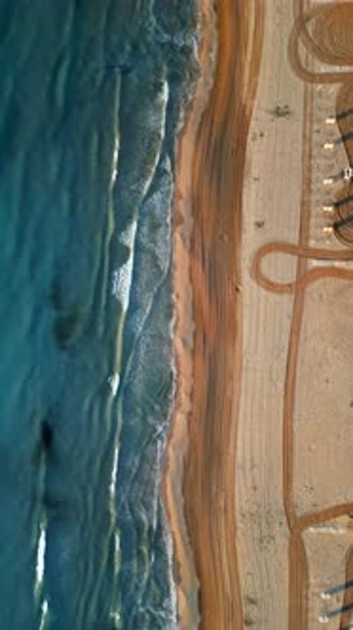Aerial drone view of waves hitting the shore on the beach in Alicante, Spain. Vertical