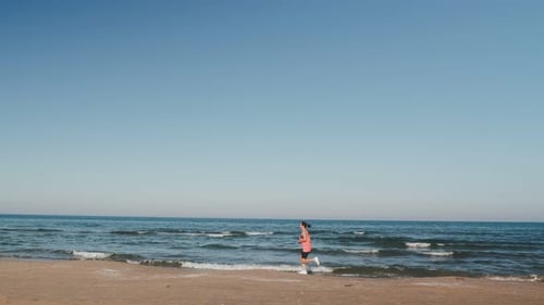Athletic fit woman running along beach at sunny morning