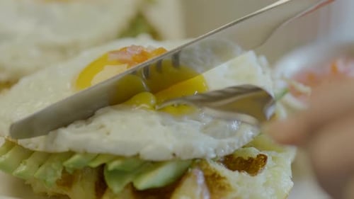 Close-up of a fried egg being cut on a waffle base with avocado