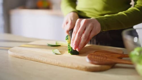 Woman Cutting Cucumber on Cutting Board in Kitchen