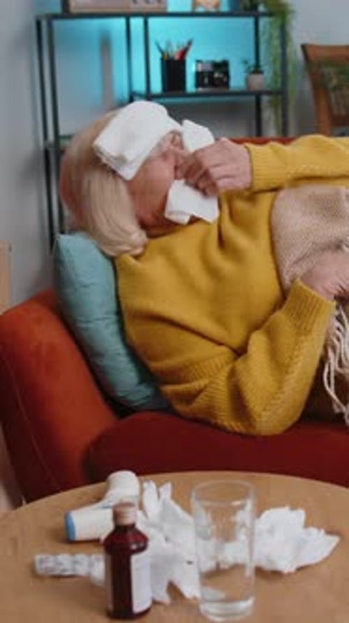 Une femme âgée malade souffrant d'une allergie au froid, allongée sur le canapé de la maison, éternue avec de la morve