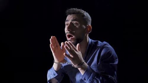 Distraught Man in Handcuffs Sits in Dark Room