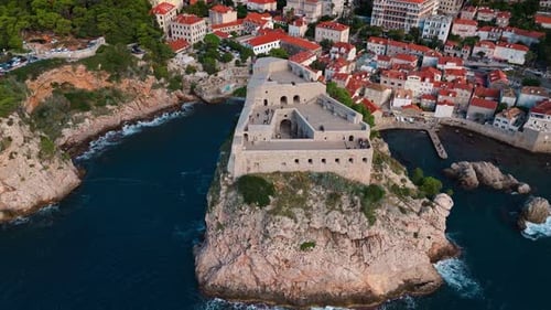 aerial wide angle panning up view of front of fort lovrjenac on Adriatic coast cliffs in blue sea