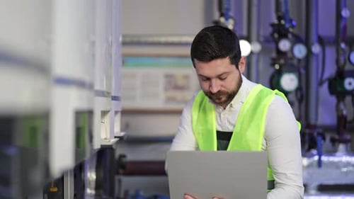 Boiler Room Worker Uses Laptop for Technical Equipment Service and Heating System Maintenance