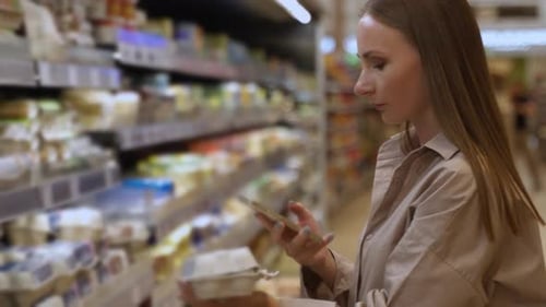 Young Woman in the Grocery Shop During Choosing and Buying Fresh Chicken Eggs She Scans the QR Code