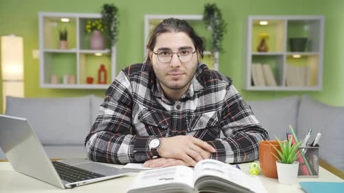Young Adult Studying with Laptop and Book at Home
