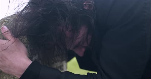 Distraught, emotional, crying man grieving the death of loved one in cemetery.