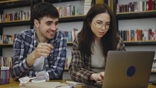 Students Collaborate on a Project in a Library Sharing Ideas While Using a Laptop and Surrounded By