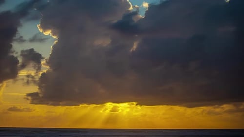 Sunset over the ocean with sunbeams through the clouds - dramatic time lapse