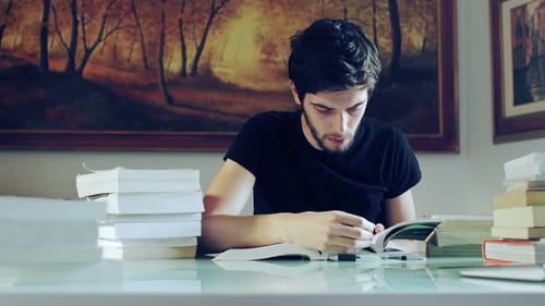 Intense Young Adult Studying at Book-Filled Table