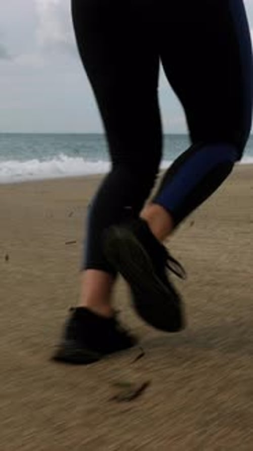 Female legs are running on sand on sea beach at stormy day. Vertical Video