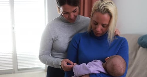 Loving lesbian moms laughing with their newborn son in their cozy USA home
