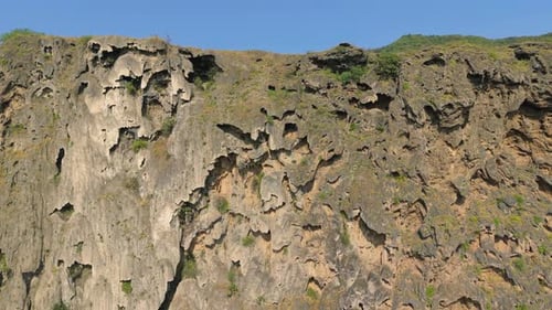 Aerial View of a Limestone Cliff Face with Natural Caves and Green Mountain Slopes Under a Clear