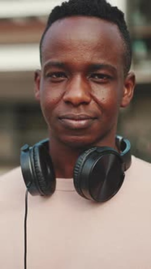 Clouse up, smiling young student stands outside of university in headphones
