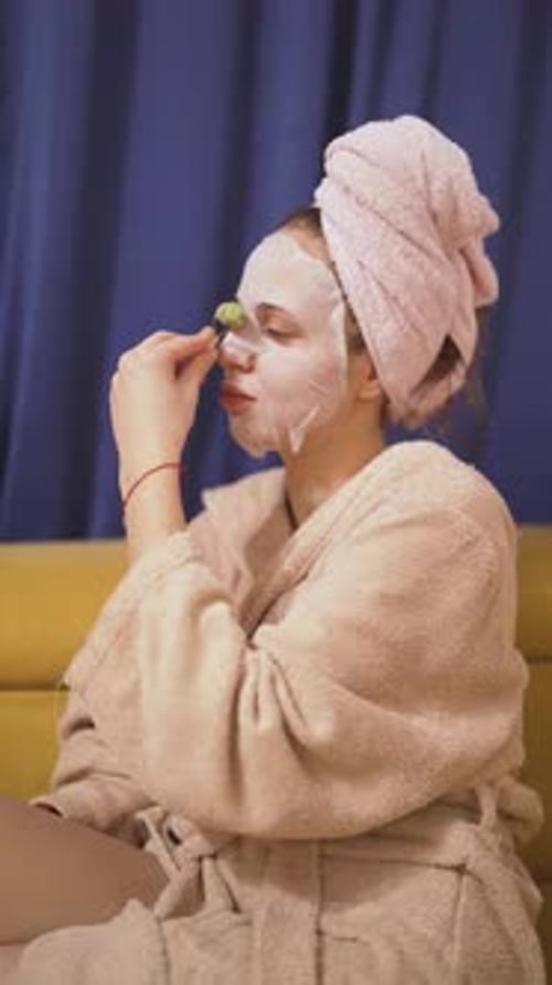Woman Applies Cucumber Slices to Face at Home