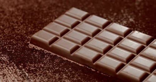 Delicious Milk Chocolate Bar on Cocoa Powder Background in Warm Light