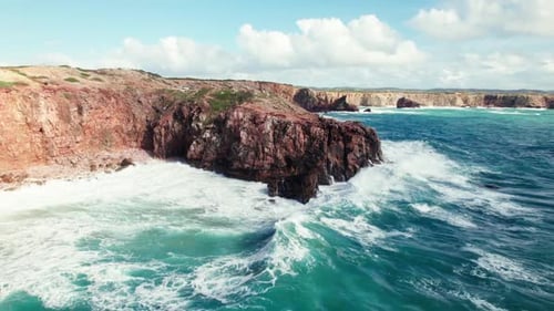 Scenic Aerial View Of Turquoise Ocean Waves Crashing Against Red Cliffs