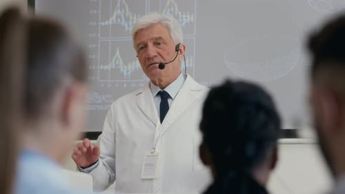 Senior Male Clinical Professor with Mic Lecturing Colleagues in Auditorium