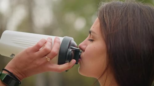 Young Woman Drinks From Water Bottle Outdoors
