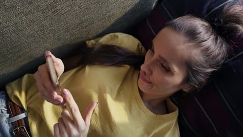 Top view of caucasian woman lying on sofa and browsing phone. Shot with RED helium camera in 8K.