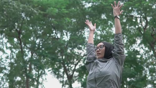 Southeast Asian hijabi woman stretching outdoors in park