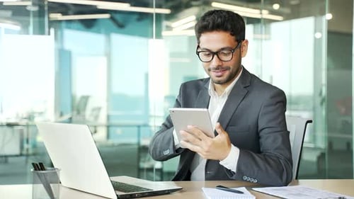Der junge Geschäftsmann in formellen Anzügen benutzt ein Tablet, während er am Arbeitsplatz im Büro sitzt. Beschäftigt