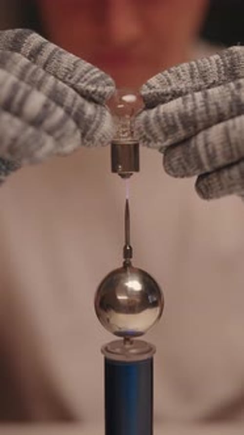 Vertikale Aufnahme eines Wissenschaftlers mit Schutzhandschuh, der eine glühende Glühbirne in der Nähe von Hochfrequenz hält