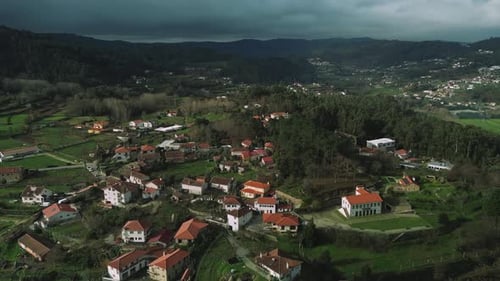 Slow push-in drone view over a small European village with red tile roofs, green hills and forest,