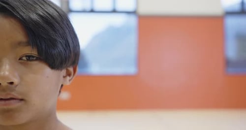 Smiling boy in school gymnasium with red wall and windows in background