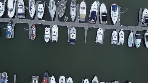 Top down aerial drone view above luxury moored private marina sailing ships and yacht boats moving f